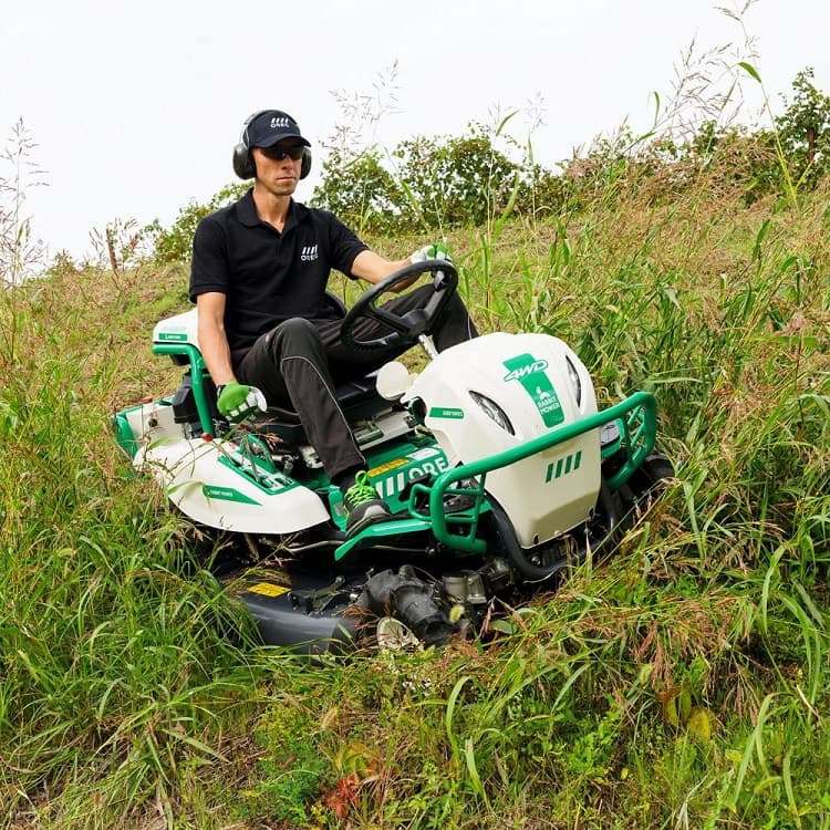 Four-wheel-drive ride-on brush mower cutting tall rough growth on a steep bank.