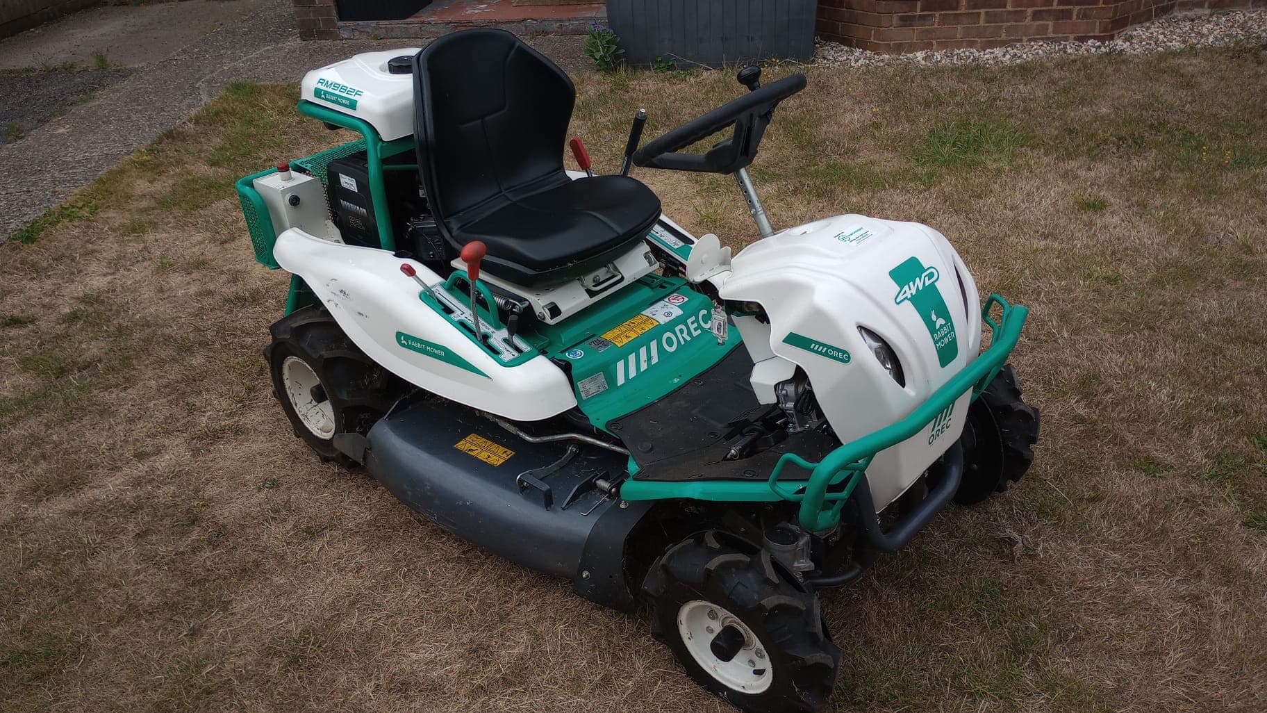 Four-wheel-drive ride-on brush mower with a rough-cut deck, standing on parched grass.