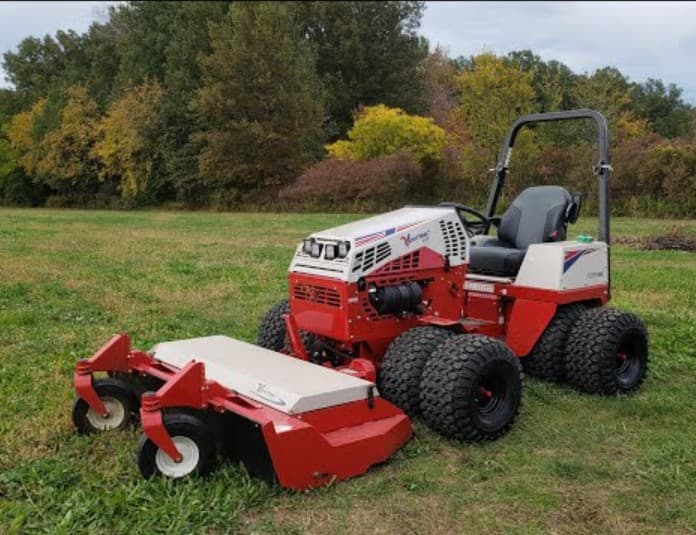 Compact articulated tractor fitted with a heavy rough-cut deck, standing on open grass.